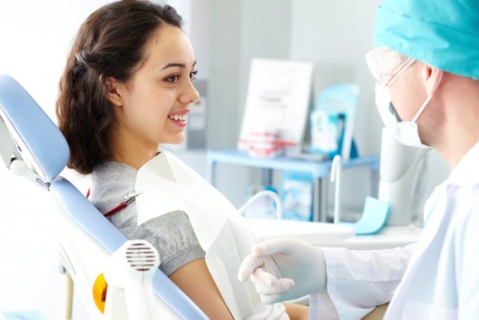 A woman sits in a dental chair talking with a dentist